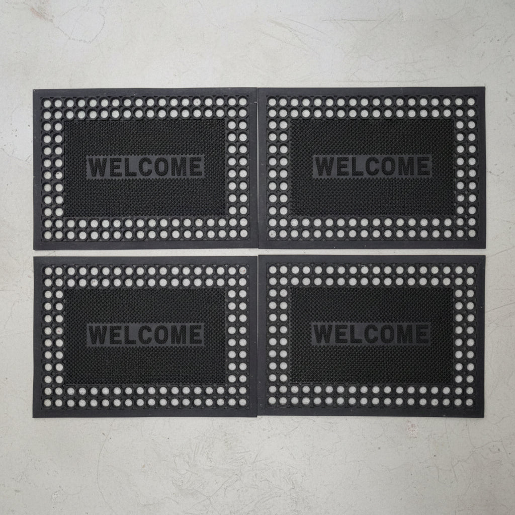 Four black doormats with 'WELCOME' text on a gray background