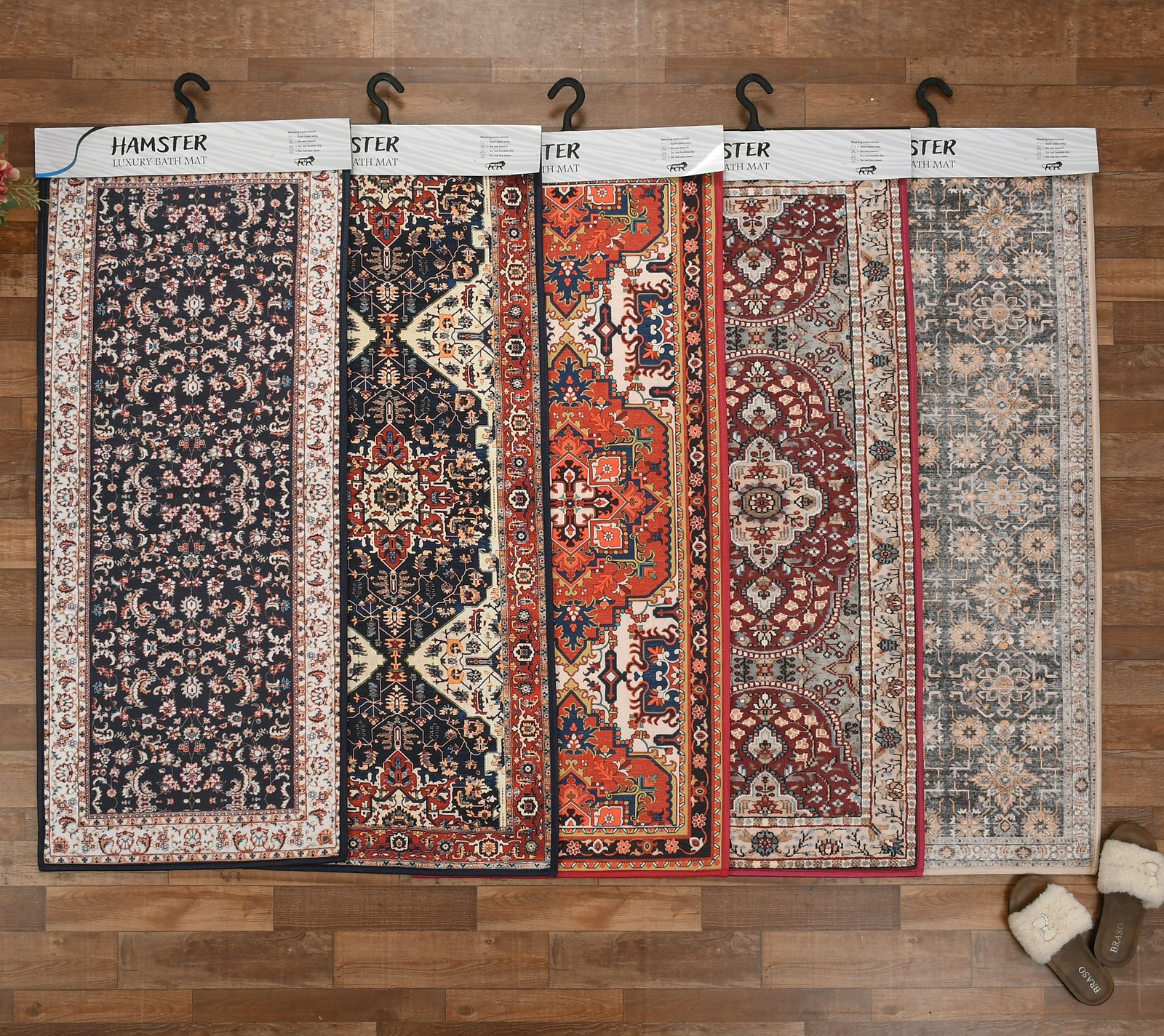 Four patterned rugs displayed on hangers against a wooden wall.