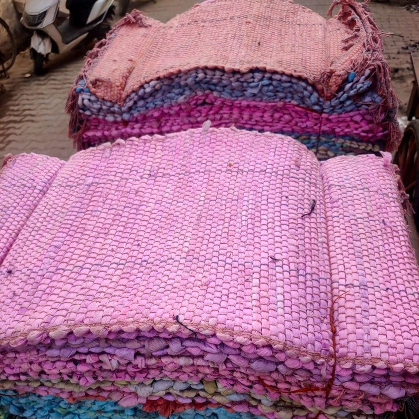 Stack of pink and multicolored woven fabric on a street.