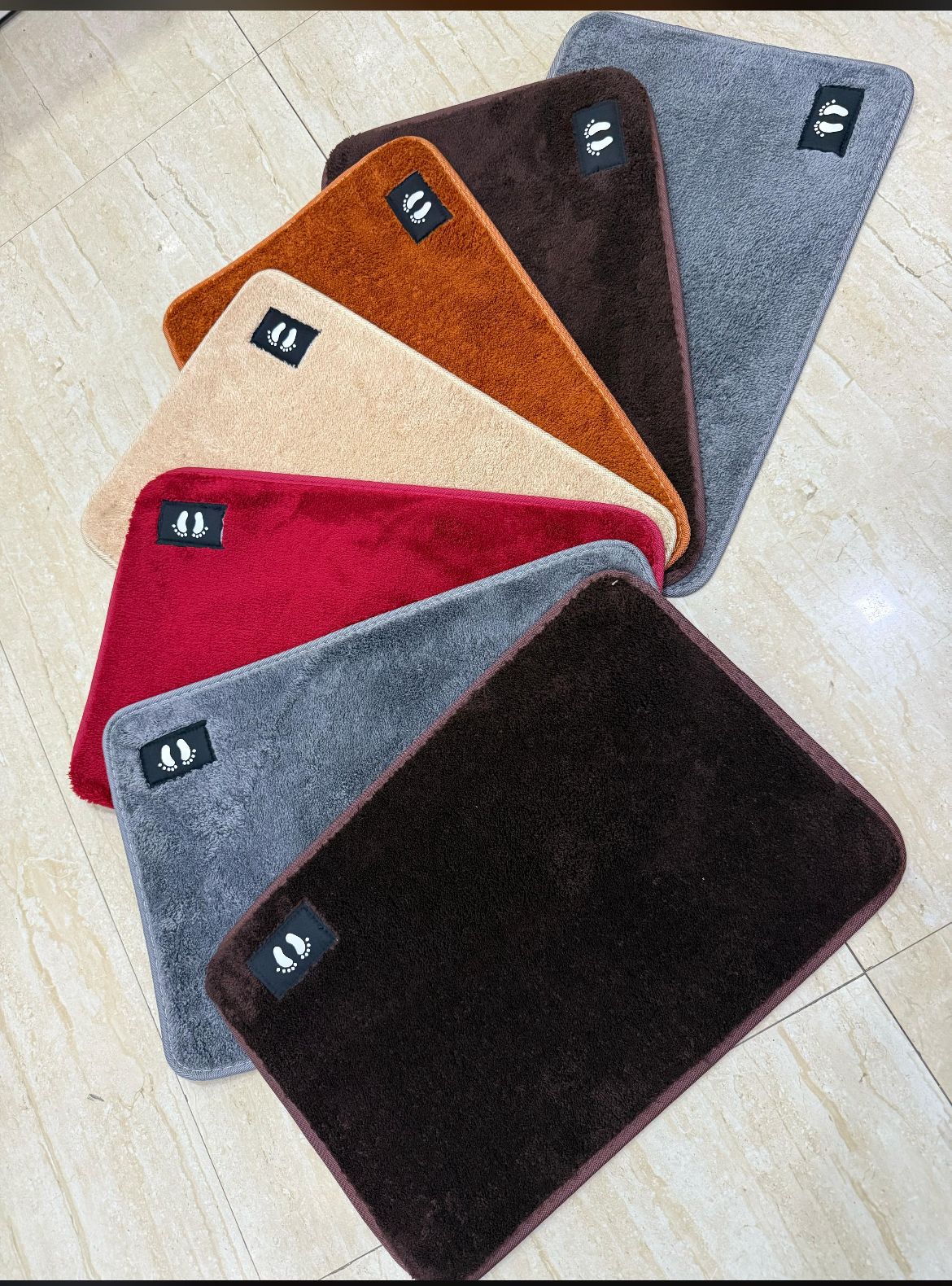 Set of six colorful bath mats on a light wooden floor.