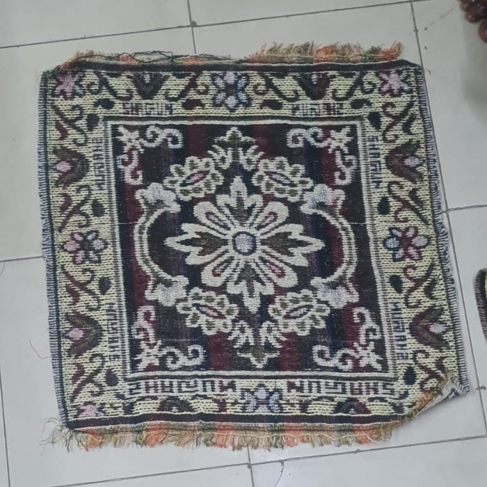 Small decorative rug on a tiled floor with feet wearing sandals around it.