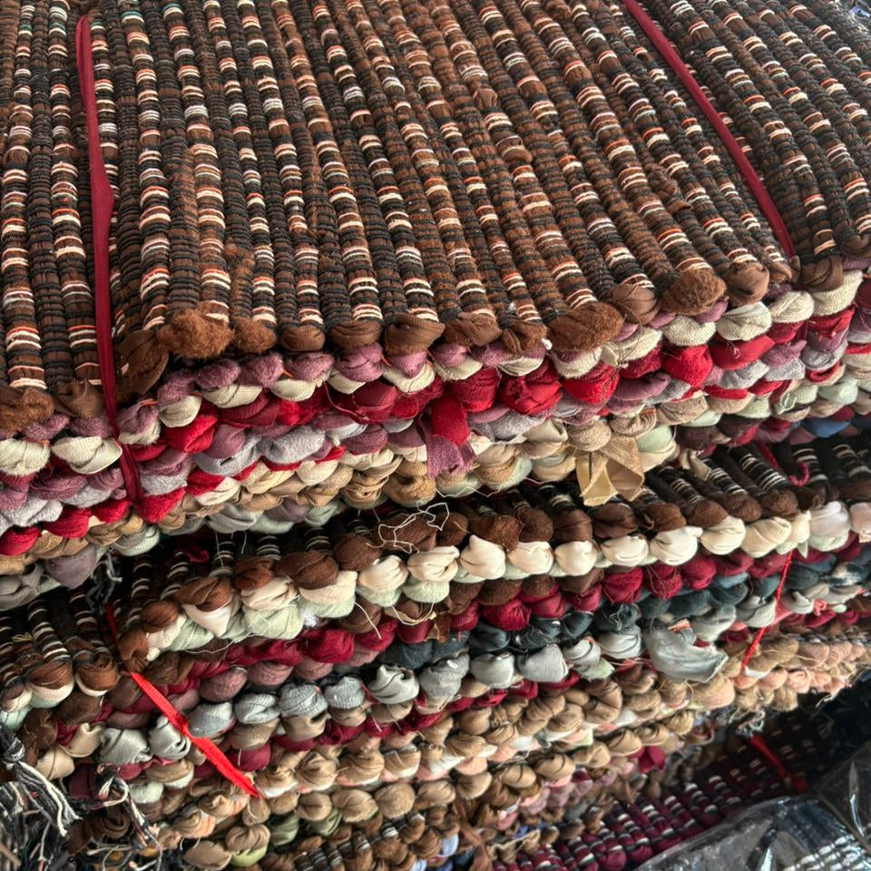 Stack of multicolored textured rugs with a focus on brown, red, and beige tones.